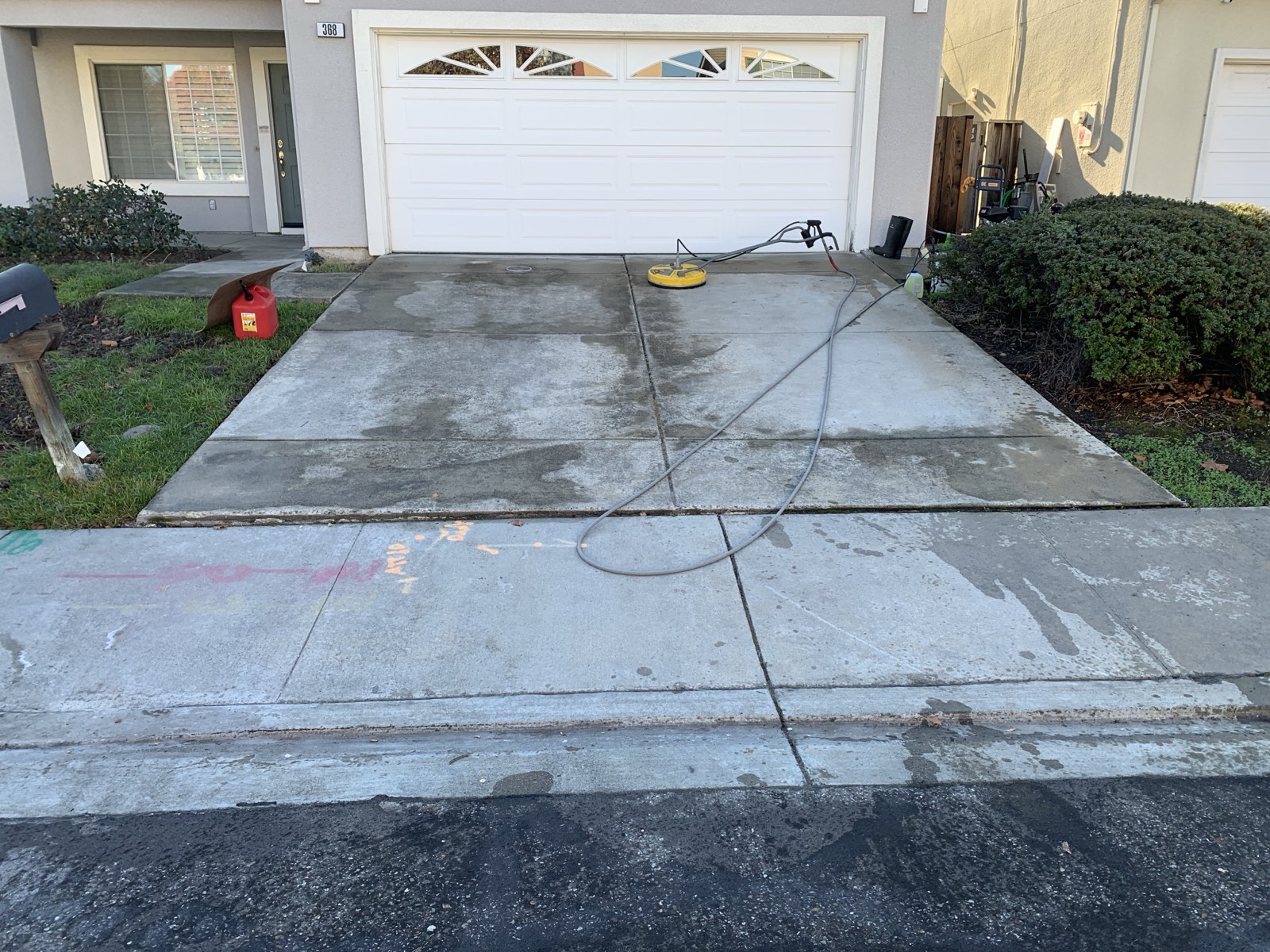 Before — full Fremont driveway with patchy dark grime in front of the white garage door, equipment staged