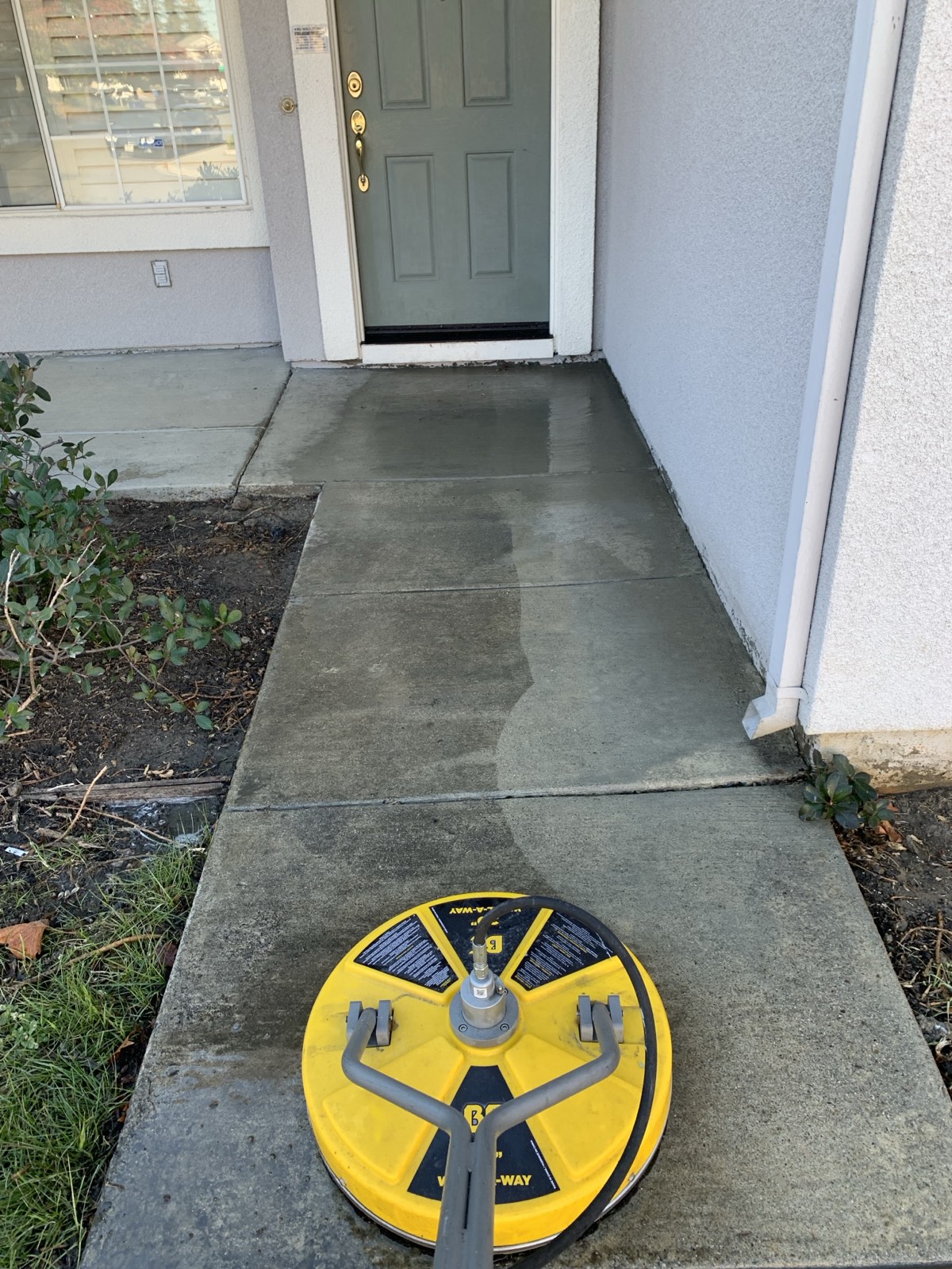 Mid-clean — rotary surface cleaner on the Fremont entry walkway, first cleaned strip against the grime