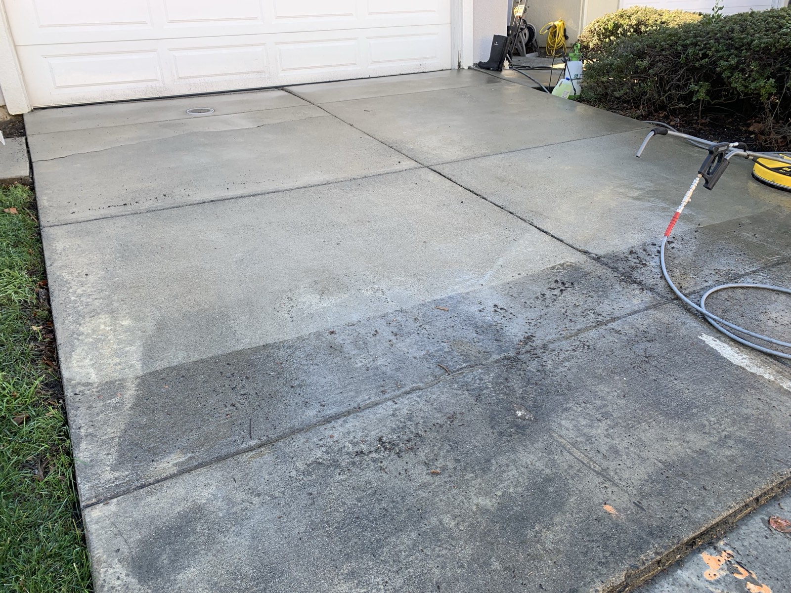 Mid-clean — Fremont driveway apron half washed, cleaned concrete against the remaining dark buildup