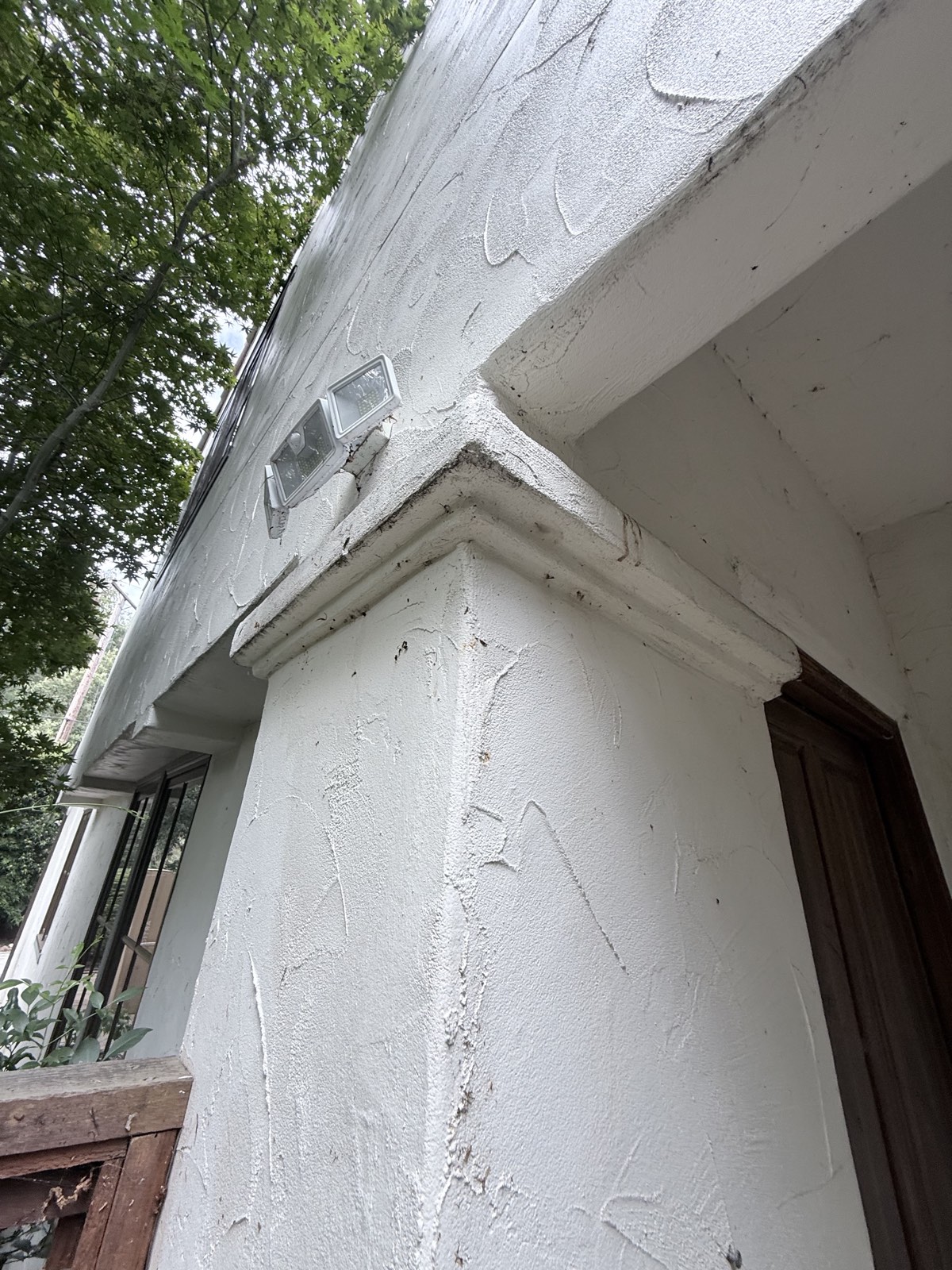 Before — Los Gatos entry column and stucco molding dotted with dark debris and cobwebs near the floodlights