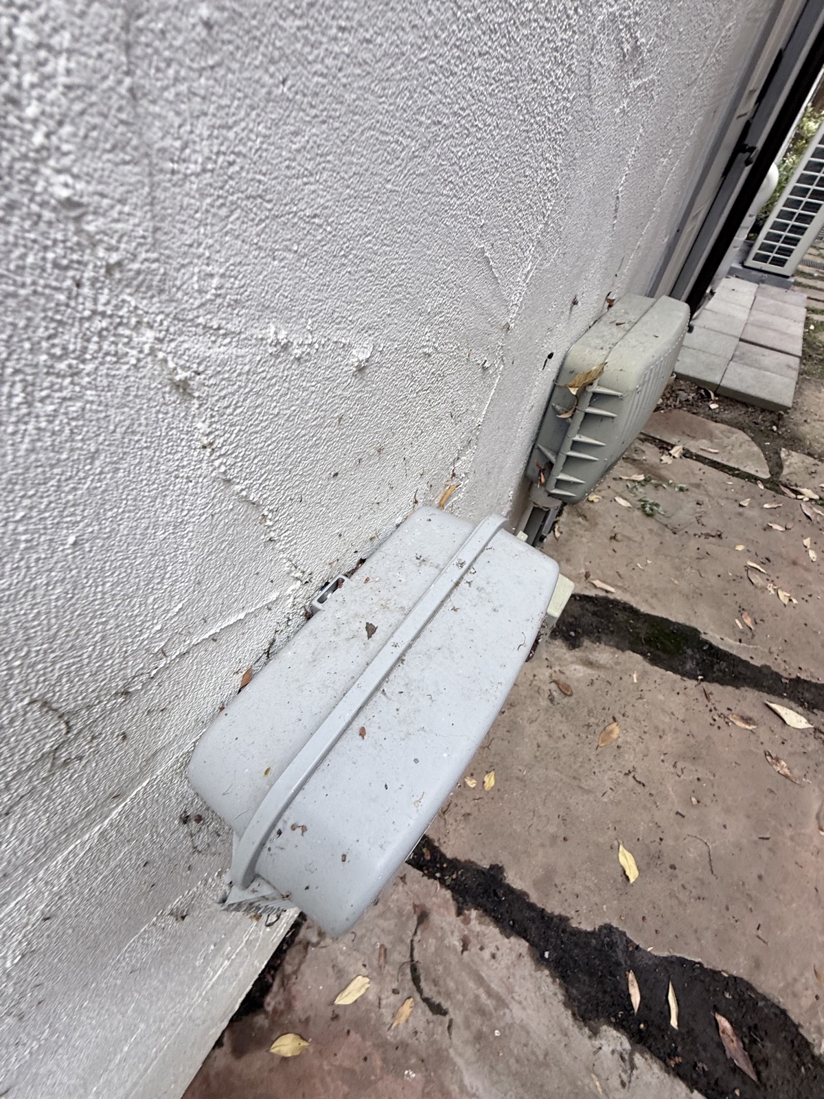 Before — utility boxes at the base of the Los Gatos stucco wall covered in dirt and fallen leaves