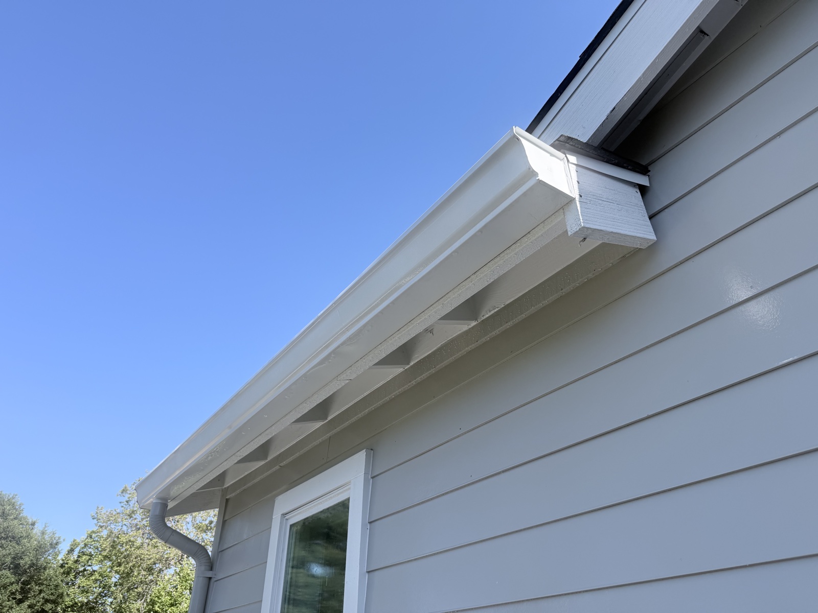 After — clean white gutter, fascia, and rafter tails over bright light gray lap siding on the Menlo Park home