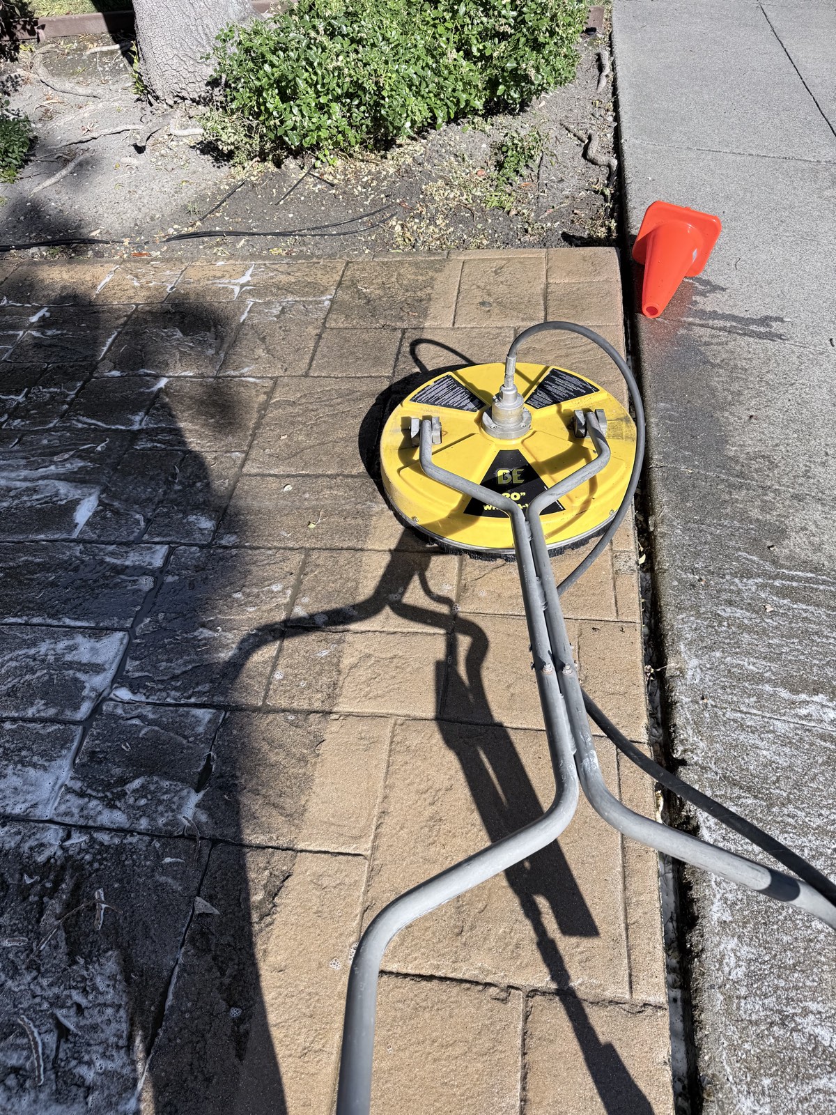 Before — surface cleaner on a grimy stamped concrete walkway at the Mountain View townhome complex, one cleaned strip showing the tan color underneath