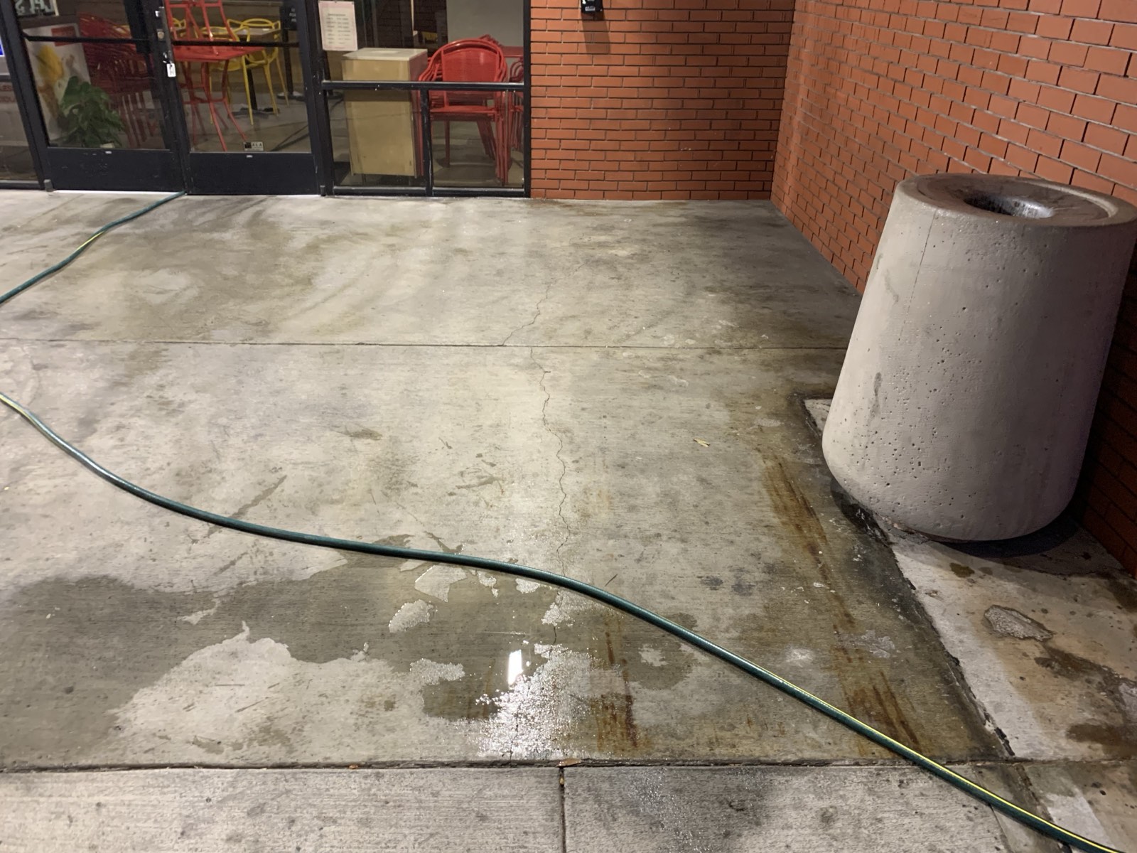 Before — stained entry concrete at a San Jose retail storefront, grime and rust streaks beside the concrete trash receptacle