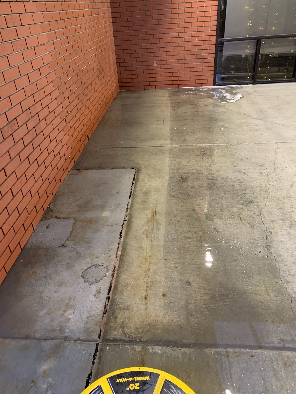 Before — walkway corner mid-wash, rust staining and buildup still visible along the brick wall
